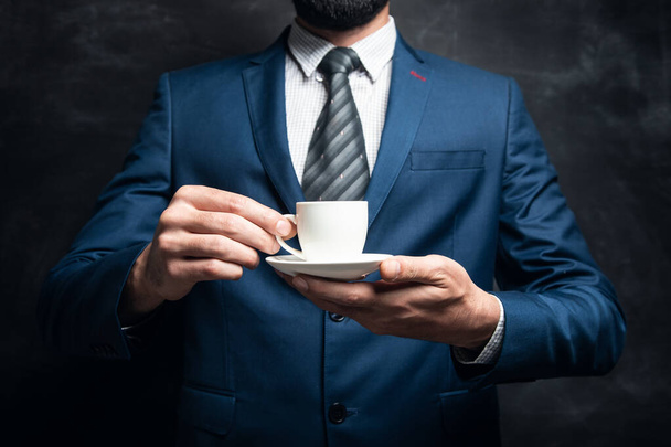 hombre de negocios sosteniendo una taza de café sobre un fondo oscuro - Foto, imagen