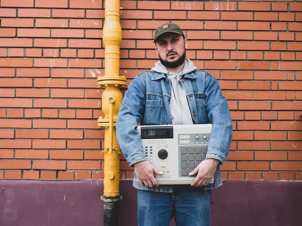 An old-school ' 90s drum machine in the hands of a beatmaker against a brick wall. Retro Digital Musical Instrument for Hip Hop Producers and Beatmakers - Fotografie, Obrázek