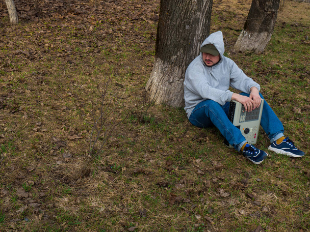 Un batteur de hip-hop est assis sur l'herbe dans un parc sous un arbre tenant une vieille machine à tambour des années 90. Instrument de musique numérique rétro pour producteurs et beatmakers de hip-hop - Photo, image