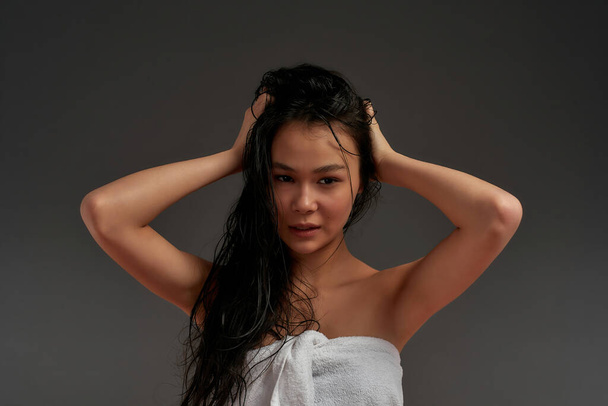 Young beautiful asian half naked woman in bath towel tousled her hair with one hand - Photo, image
