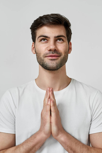 Young bearded man wearing t-shirt praying - Фото, изображение