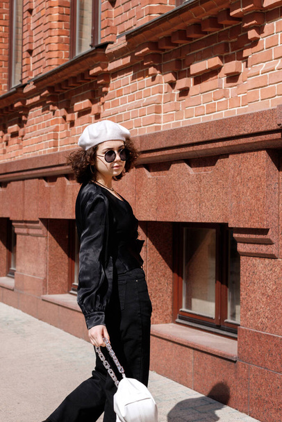 chica en gafas y boina blanca fuera del edificio en un paseo - Foto, Imagen