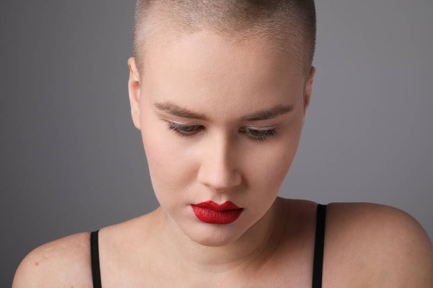 Close-up of young woman with shaved hairstyle, posing over grey background. - Foto, imagen