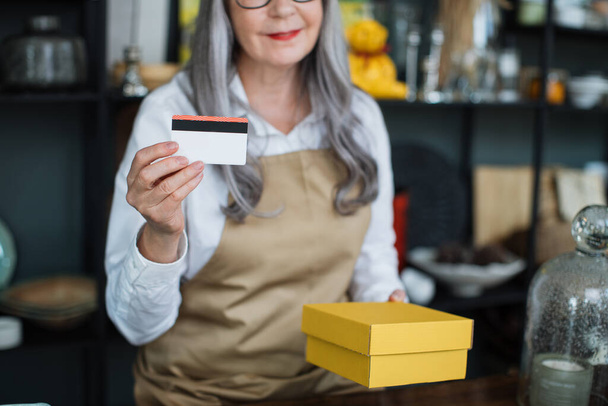Close up of aged saleswoman holding credit card and box - Фото, зображення