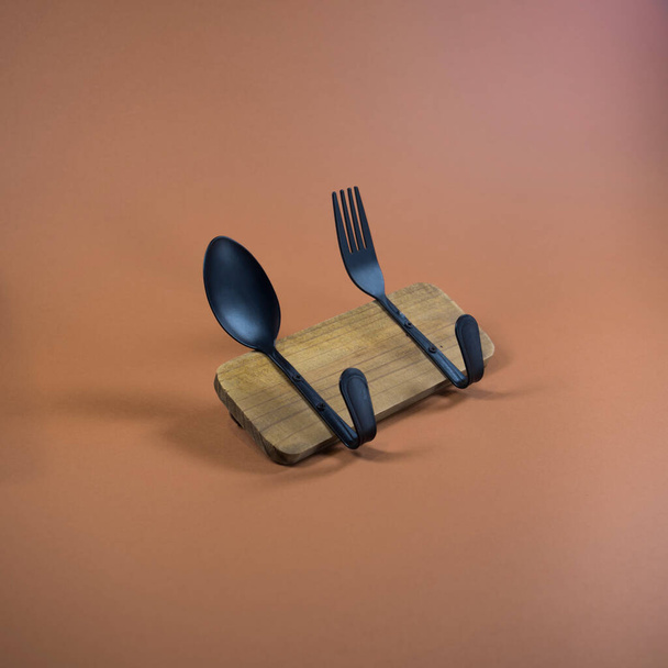 Kitchen hook made of spoon and fork attached to wooden tile. Brown, orange background. Minimal abstract composition. Food, drinks, interior idea.  - Φωτογραφία, εικόνα