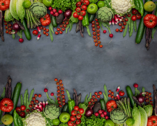 Verschillende biologische groenten - asperges, tomaten kers, avocado, artisjok, peper, limoen, citroen, zout op grijze achtergrond. Rauw veganistisch vegetarisch concept. - Foto, afbeelding