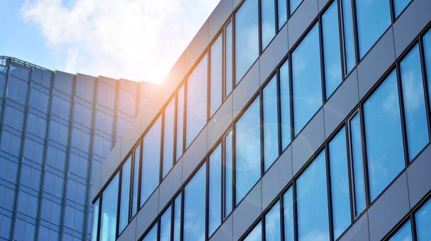 Blauwe lucht reflectie in glazen gevel van het gebouw. Uitzicht op kantoorgebouw ramen close-up met zonsopgang, reflectie en perspectief.. Glazen gevel op een heldere zonnige dag met zonnestralen aan de blauwe hemel.  - Foto, afbeelding