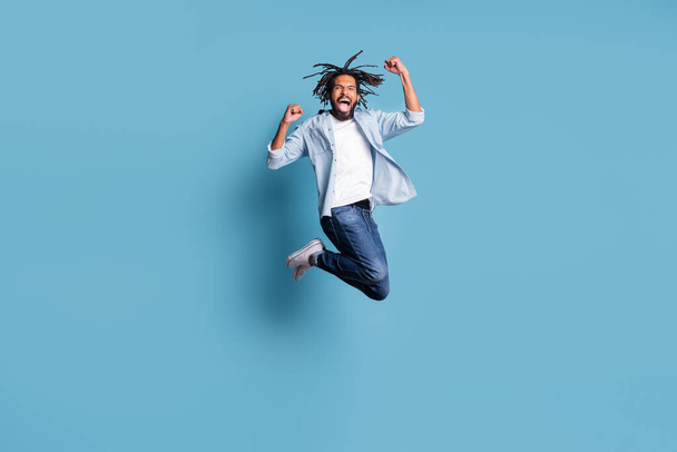 Full length photo of astonished dark skin person jumping fists up open mouth celebrate isolated on blue color background - Valokuva, kuva