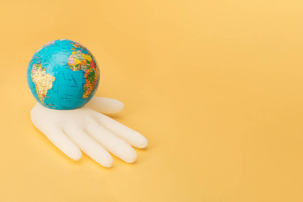 A white inflatable surgical glove holds a globe. Golden background. Minimal. - Photo, Image