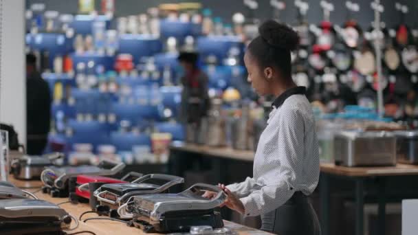 giovane donna afro-americana è lo shopping in negozio di elettrodomestici nel centro commerciale, scegliendo griglia elettrica - Filmati, video