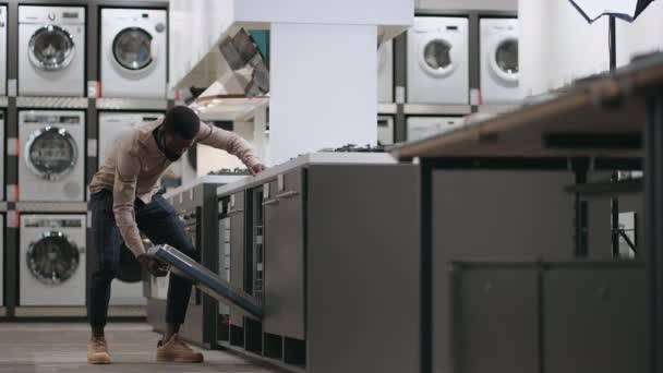 чорний хлопець дивиться посудомийну машину в торговельній зоні сучасного магазину побутової техніки, відкриваючи двері і оглядаючи всередині
 - Кадри, відео