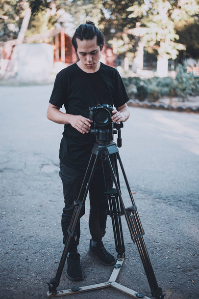 Stylischer junger Operator in Schwarz arbeitet im Freien mit einer Kamera - Foto, Bild