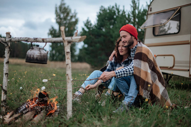Casal em um xadrez xadrez assando marshmallows em chamas perto da casa de reboque. - Foto, Imagem