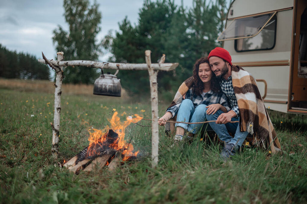 Couple in a checkered plaid roasting marshmallows on fire near the trailer home. - Photo, Image