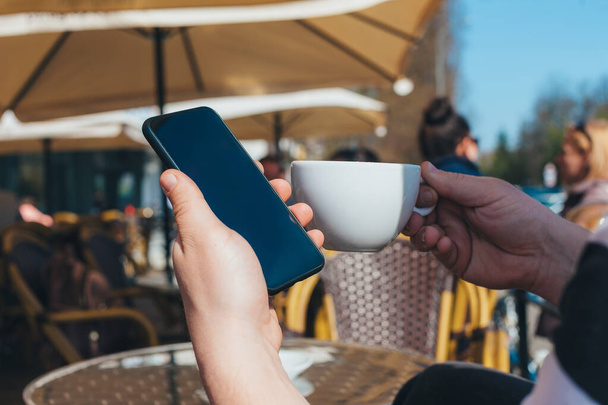 Man holds a smartphone on the background of a cup of coffee in a restaurant - Фото, зображення