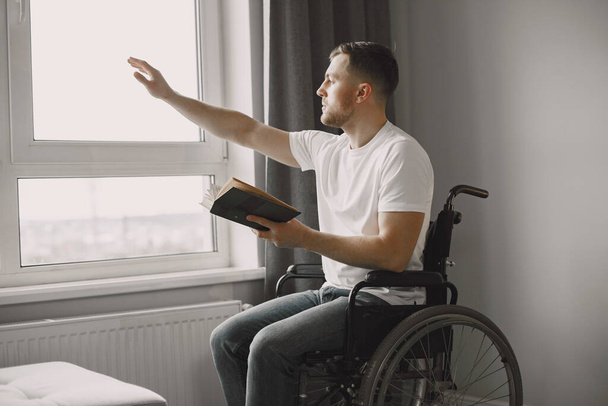 Handicapped man in wheelchair reading a book at home - Φωτογραφία, εικόνα
