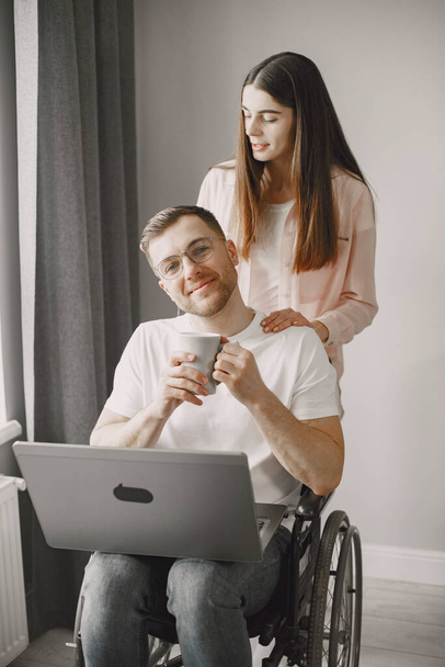 Young man in wheelchair using laptop and girlfriend hugging him at home - Foto, imagen