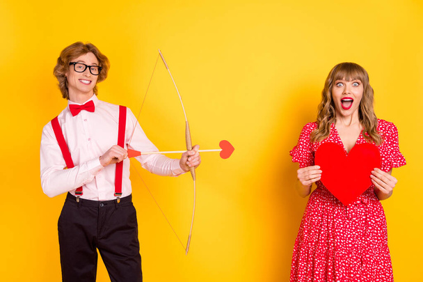 Photo portrait of guy with arrow bow and amazed girl keeping red heart isolated on vibrant yellow background - Foto, immagini