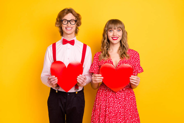 Photo portrait of boy and girl keeping red heart shaped postcards on date isolated on vibrant yellow background - Фото, изображение