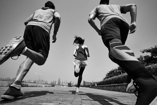 trois jeunes asiatiques adultes courir jogging à l'extérieur, vue arrière et basse angle, noir et blanc - Photo, image