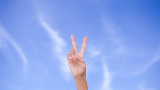 Sottile donna mano due dita mostrando isolato su immagine sfocata del cielo blu. forza, nuovo inizio, vittoria, incoraggiamento, La lotta, nuova speranza, concetto di simboli di successo. - Foto, immagini