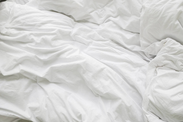 wrinkle messy blanket and white pillow in bedroom after waking up in the morning, from sleeping in a long night, details of duvet and blanket, an unmade bed in hotel bedroom with white blanket. - Foto, imagen