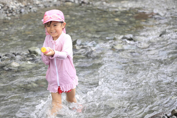 Japońska dziewczyna bawiąca się w rzece z pistoletu wodnego (5 lat) - Zdjęcie, obraz