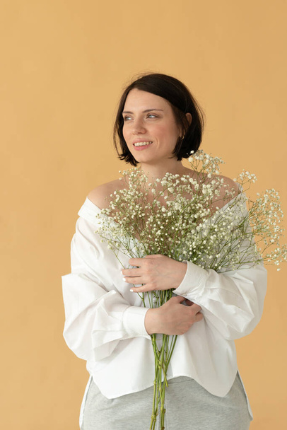 retrato de una joven mujer hermosa en el estudio con flores blancas sobre un fondo amarillo - Foto, Imagen
