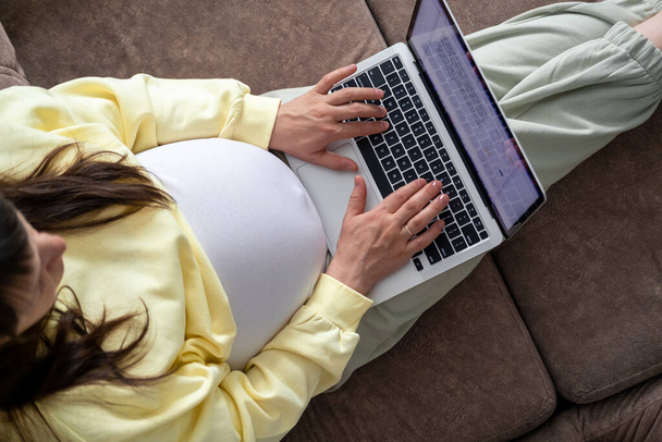 Attractive pregnant young lady working remotely online from home. Close up woman hands on laptop with big belly advanced pregnancy - Фото, изображение