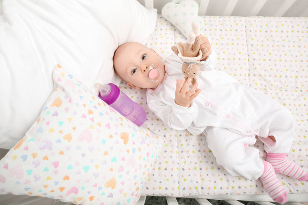 Lindo bebé con biberón de agua y juguete en cuna - Foto, Imagen