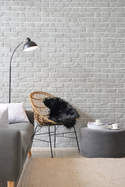Fauteuil moderne avec pouf et lampe près du mur de briques dans le salon - Photo, image