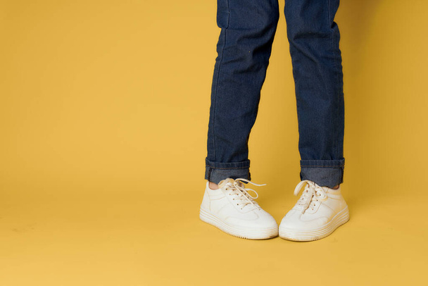 damskie nogi dżinsy biały trampki moda ulica styl żółty tło - Zdjęcie, obraz