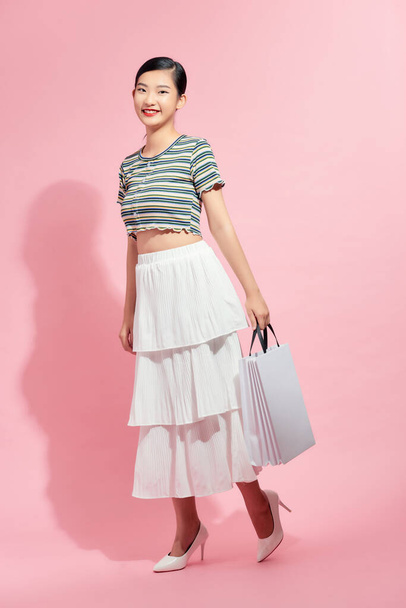 full length view of cheerful, fashionable woman holding white shopping bags and smiling on pink background - Photo, Image