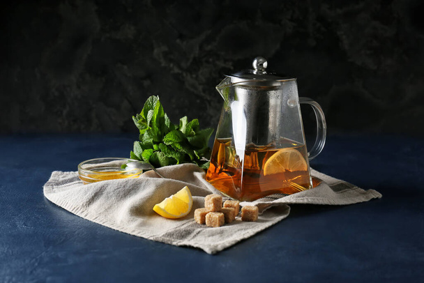 Tetera de té sabroso con limón, miel y menta sobre fondo oscuro - Foto, imagen