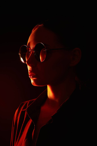 Красива молода жінка в сонцезахисних окулярах. Модна дівчина в червоному світлі
 - Фото, зображення