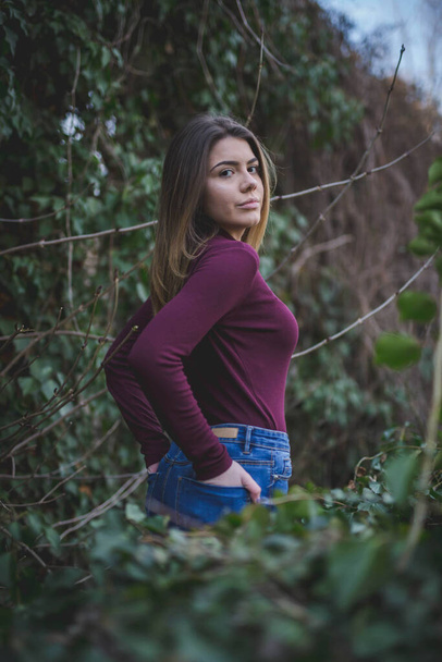 A shallow focus of an adult woman wearing a sweater with jeans in a park covered in greenery - Photo, image