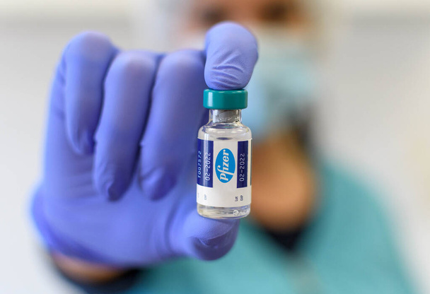 ZAGREB, CROATIA - Apr 16, 2021: Cropped selective focus image of hand in glove holding vaccine vial with pfizer logo. - Fotografie, Obrázek