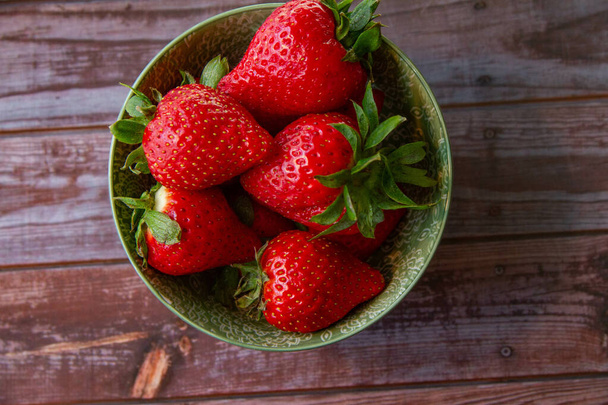 A top view of juicy fresh strawberries in a green bowl on a wooden surface - Φωτογραφία, εικόνα