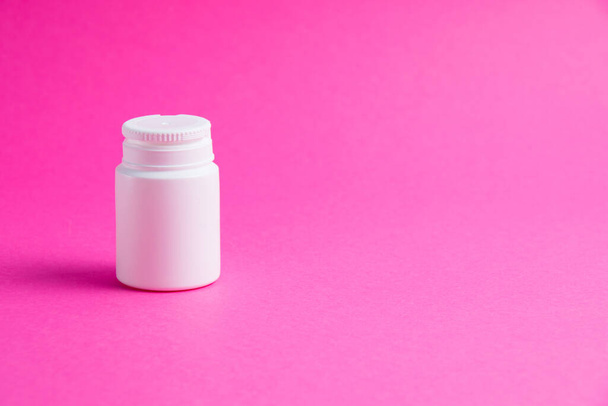 Vasetto bianco di pillole o vitamine su sfondo di carta rosa. Medicina su sfondo con spazio di copia - Foto, immagini