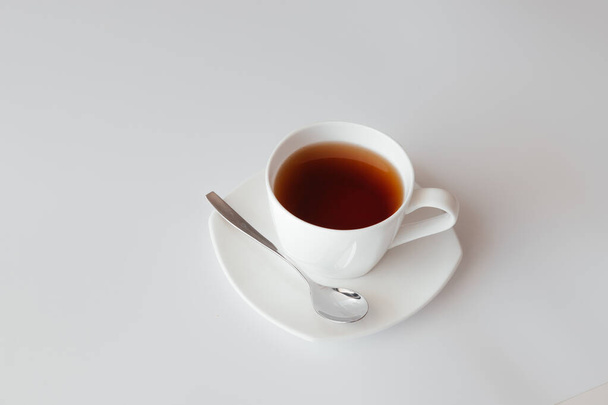 Eine weiße Tasse Tee mit Untertasse und Löffel auf weißem Hintergrund. Draufsicht auf Kaffeebecher. Nettes Banner für Café-Menü oder Restaurant. Morgens Frühstück. Mit Kaffee in den Tag starten - Foto, Bild