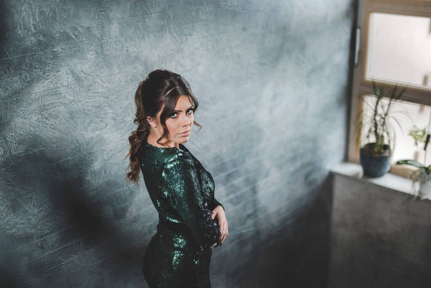 A sexy Bosnian brunette girl in stylish green sequins dress standing on the stairs looking up - 写真・画像