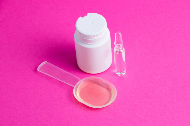 Ampoule avec médicament, mélange médicinal et pot blanc de pilules sur fond rose. - Photo, image