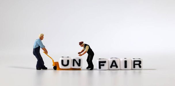 Two miniature men moving the cube of 'UN' word from cube with 'FAIR' word to cart. White cube with words and miniature people. - Photo, Image