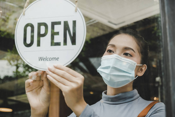 Open. waitress staff wearing protection face mask turning open sign board on glass door in modern cafe coffee shop, cafe restaurant, retail store, small business owner, food and drink concept - Foto, Bild
