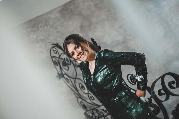 A shallow focus shot of a beautiful Caucasian woman in a shiny green dress, posing indoors in a decorative stairwell - Photo, image