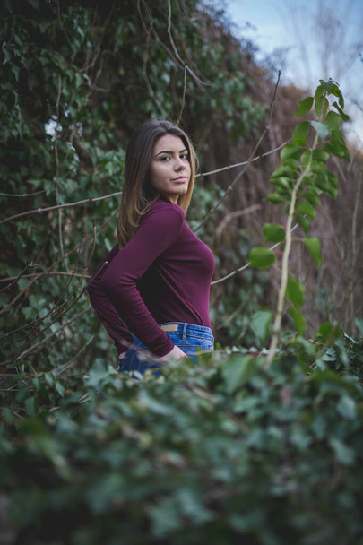 A vertical shot of an attractive female posing in the middle of the trees in a park - 写真・画像