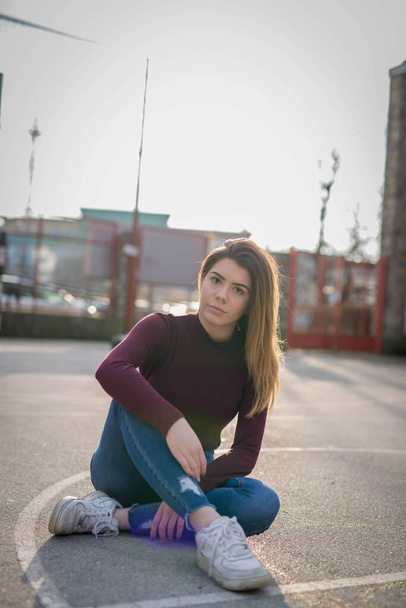 A shallow focus of an adult woman wearing jeans with a sweater and sitting on a football pitch in a yard - Foto, Imagen