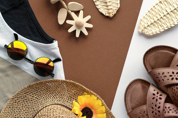 Natural brown earth colored summer autumn female fashion outfit. Flat lay, top view on split two tone paper background. Straw leaves, sunglasses, straw hat, geometric shirt, flower, leather sandals. - Φωτογραφία, εικόνα
