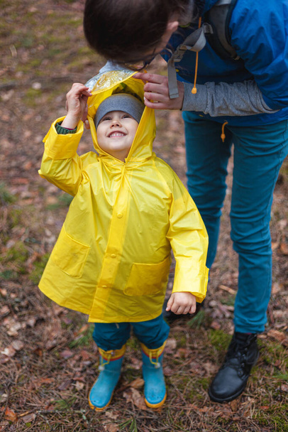 Äiti ja lapsi kävelevät metsässä sadetakkien sateen jälkeen yhdessä, äiti laittaa sadetakin. - Valokuva, kuva