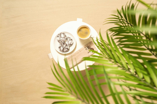 Cup of coffee with chocolate cookies on the table under palm trees on the sandy beach. Outdoors cafe. Top view - 写真・画像